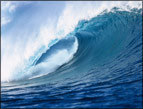 blue ocean wave cresting with white foam blowing off the cap of the wave